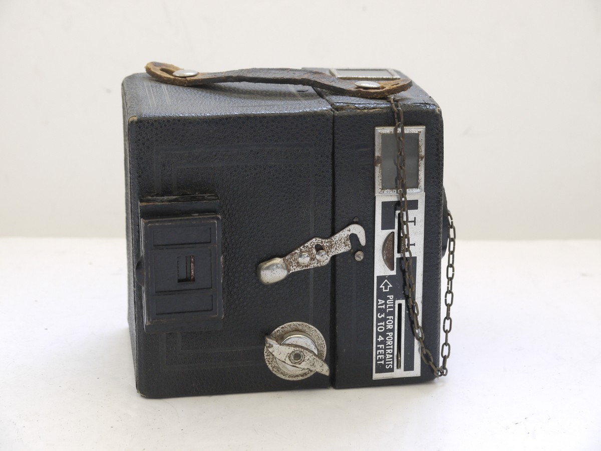 mwclassiccameras-20210716-276 Kodak Six-20 Brownie Junior leatherette covered Box camera, all plain, with added side mounting sports finder & front cap on a chain with metallic Art-Deco patterned front c1934-42. No handle