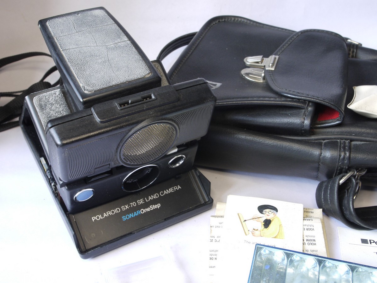 mwclassiccameras-20220729-266 Polaroid SX-70SE Sonar Onestep folding polaroid land camera with strap, flash bar, strap, "The artist at work" card, instructions & kodak case. Also with 3-image special effects filter for the Polaroid Impulse camera. THE PROPERTY OF THE LATE BERYL REID, ACTRESS (But no Provenance available - bought at auction of her possessions