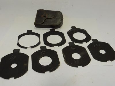 Unamed Waterhouse Stops set of Seven Metal Stops with notch/cut-out at the end. Marked f3.5, f4.8, f5.6, f7, f10, f17 & f13.5 (80x65mm), with end handle grip & Brown leather case. Apparently for use with a Clement & Gilmer Petzval lens c1893