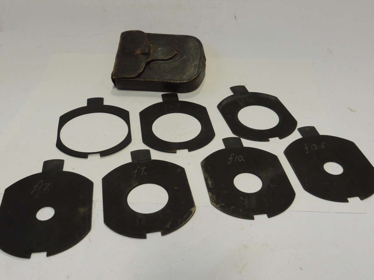 mwclassiccameras-20241129-90 Unamed Waterhouse Stops set of Seven Metal Stops with notch/cut-out at the end. Marked f3.5, f4.8, f5.6, f7, f10, f17 & f13.5 (80x65mm), with end handle grip & Brown leather case. Apparently for use with a Clement & Gilmer Petzval lens c1893