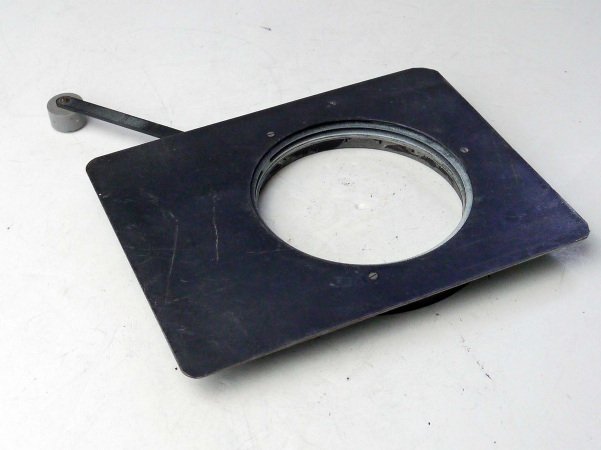 mwclassiccameras-20250404-61 Unbranded Vintage Iris Diaphragm, adjusted with extended lever arm. On a metal panel. Widest Diameter is 70mm. Panel is 150 x 115mm