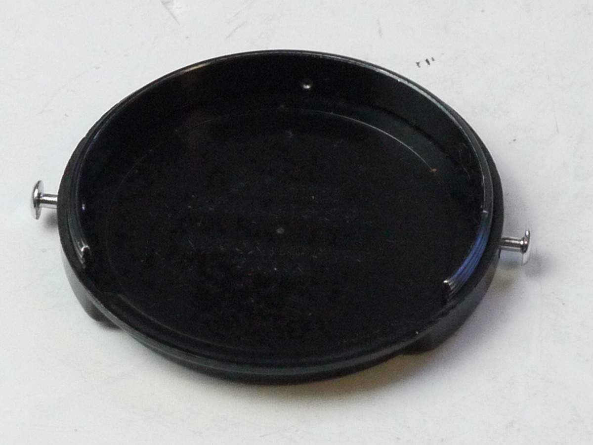 mwclassiccameras-20250704-286 Nippon Kogaku Hard plastic Clip-on front lens cap, marked "Nikkor" with metal "ears"