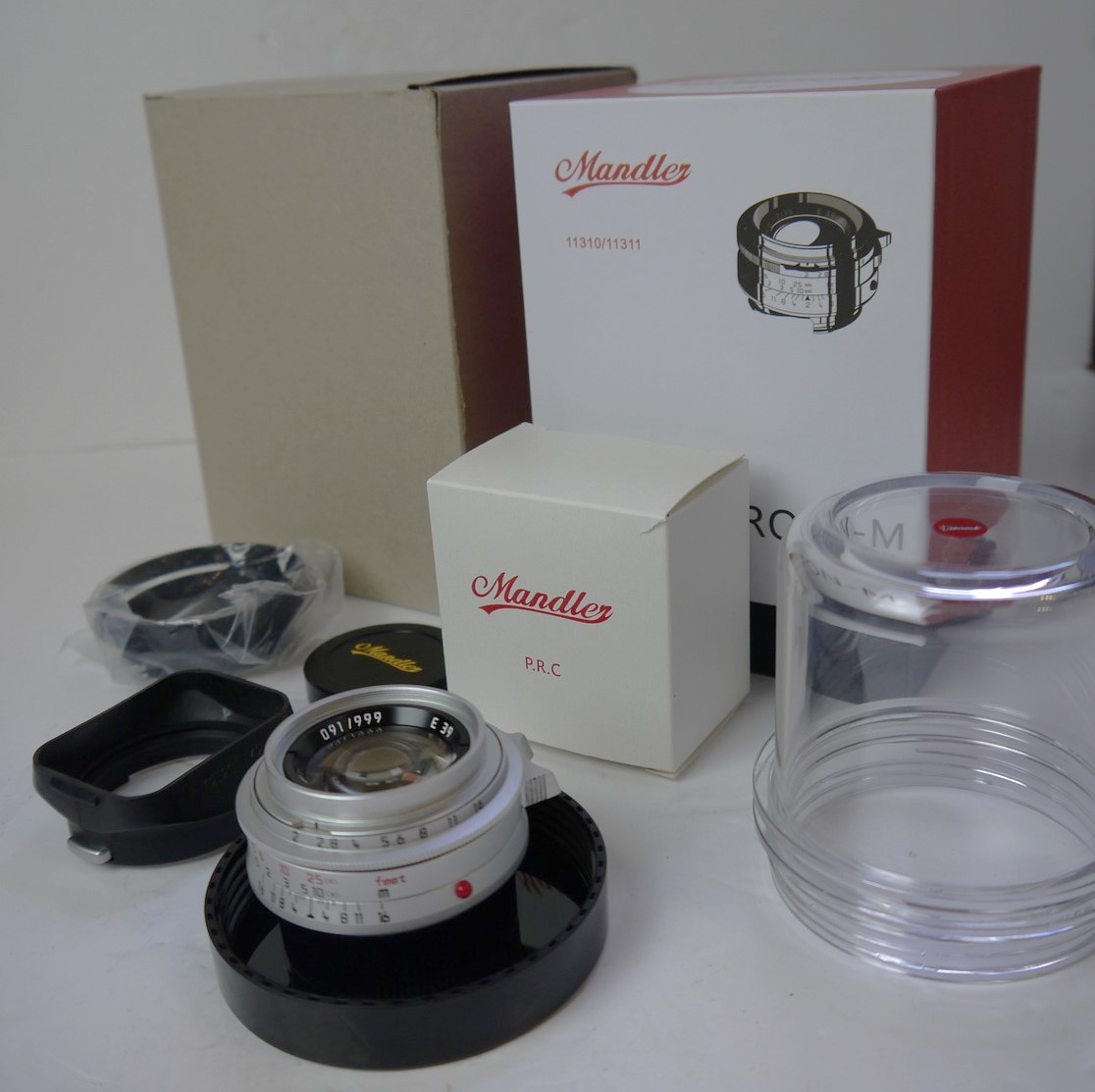 mwclassiccameras-20250926-41 Mandler 35mm f2 7-Element Chrome lens based on the Leica 35mm f2 Summicron-M lens. A Well-Regarded, Quality-made lens with very nice bokeh, Made in China in Leica M mount + Mandler front cap, A42 Clip-On square plastic lens hood, Clip-On metal lens with vents, Keeper case, Hood/filter Box & main Box with packaging & outer box. No.91 out of 999